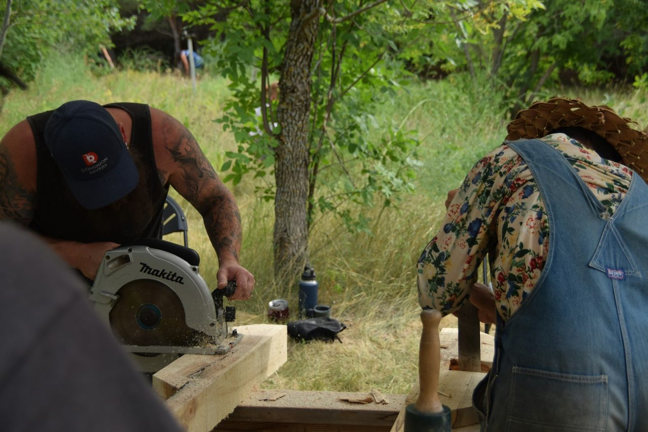 Two people cutting timber outdoors with a circular saw, building a frame.